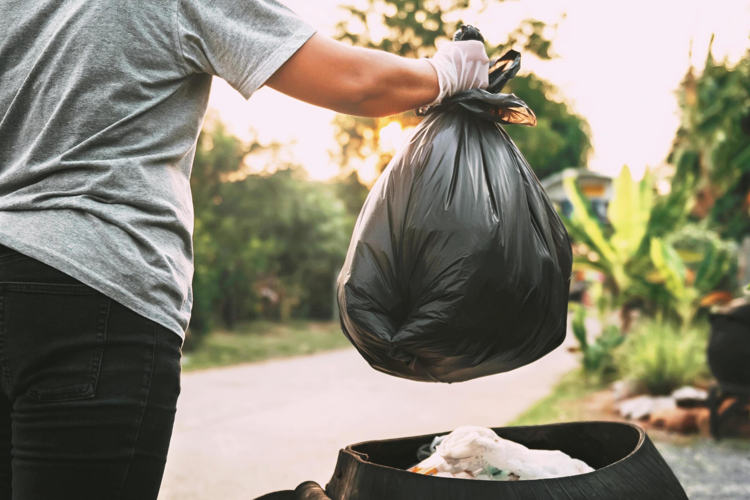 hand-holding-garbage-black-bag-putting-in-to-trash-free-photo